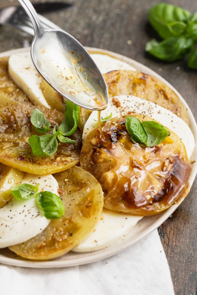 Balsamic vinaigrette being drizzled over grilled green tomatoes and slices of mozzarella.