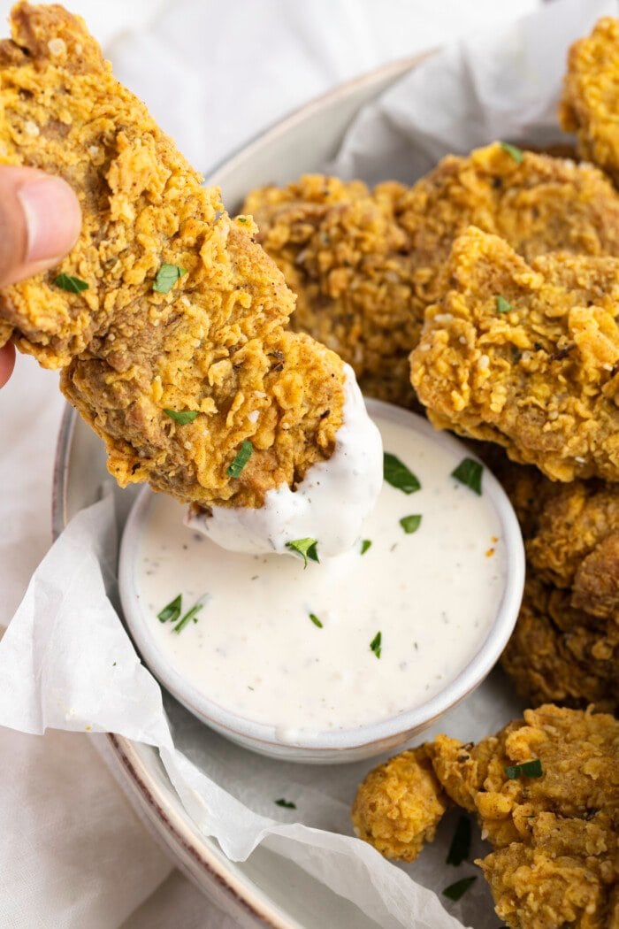 Seitan fried "chicken" tender being dipped into a small ramekin of vegan ranch dressing.