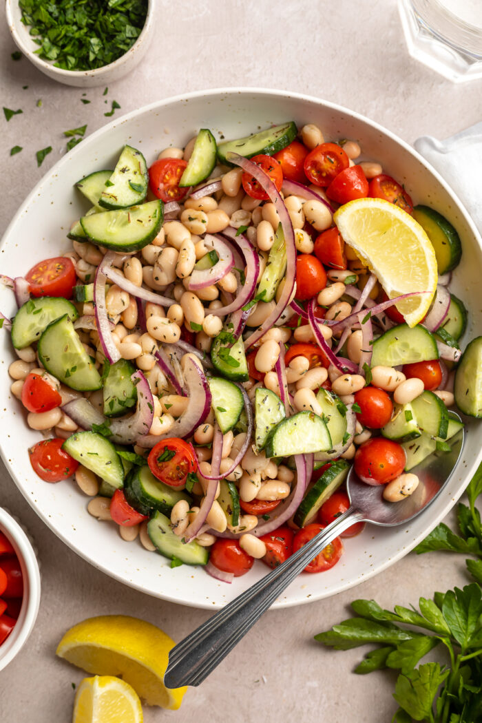 Overhead photo of a white bowl of white bean salad on a white tablescape.