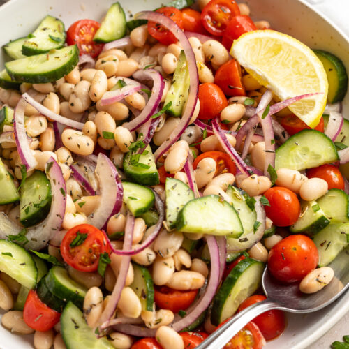 Overhead, 3/4-angle view of white bean salad in a large white bowl with a spoon.