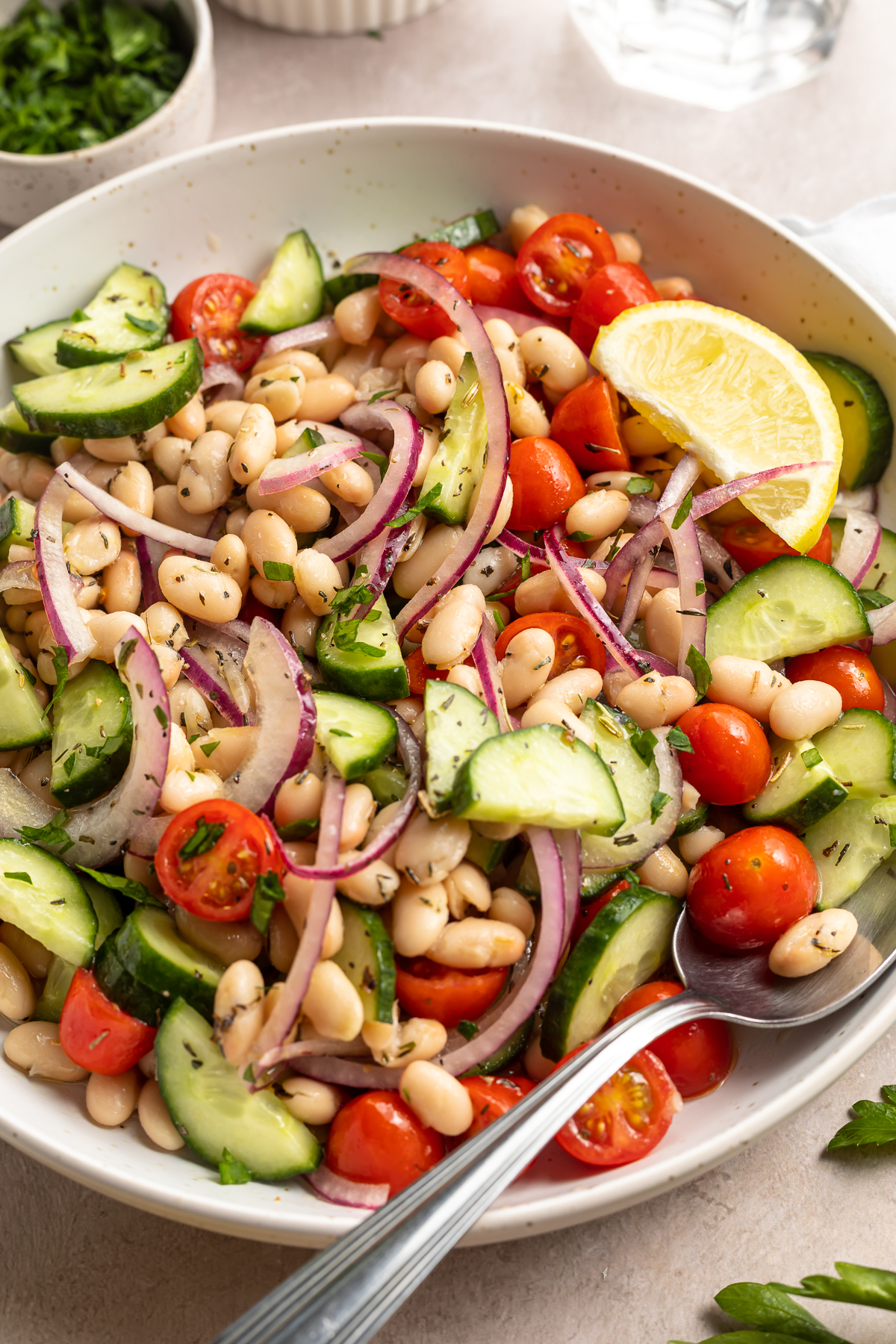 Overhead, 3/4-angle view of white bean salad in a large white bowl with a spoon.