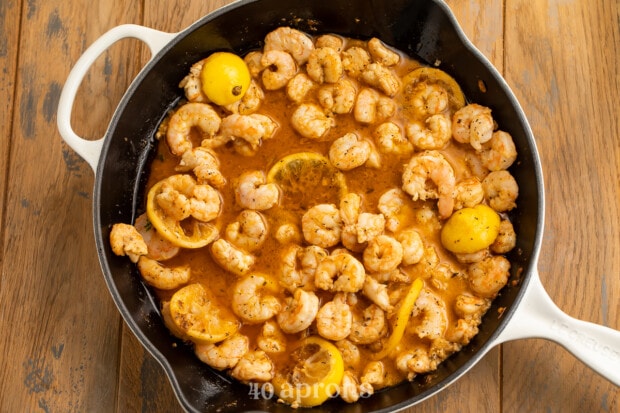 Overhead view of buttery BBQ shimp in a large skillet with lemon slices.