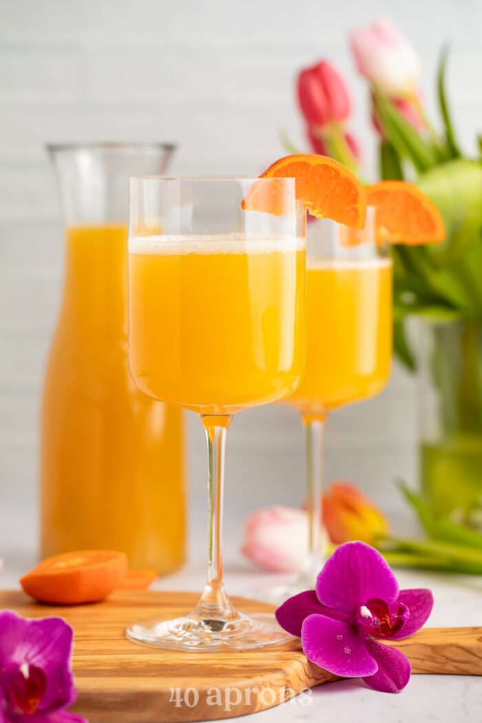 Side view of two wine glasses holding POG juice mimosas with a carafe of pog juice in the background.