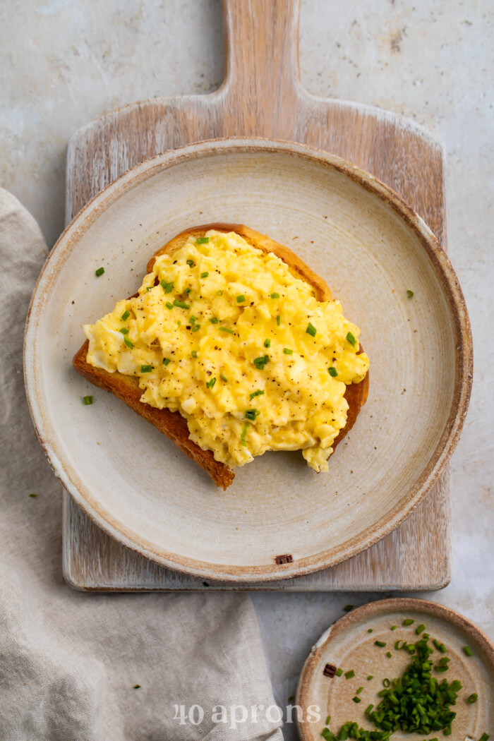 Overhead view of truffled scrambled eggs on toast on a plate resting on a wooden serving board.