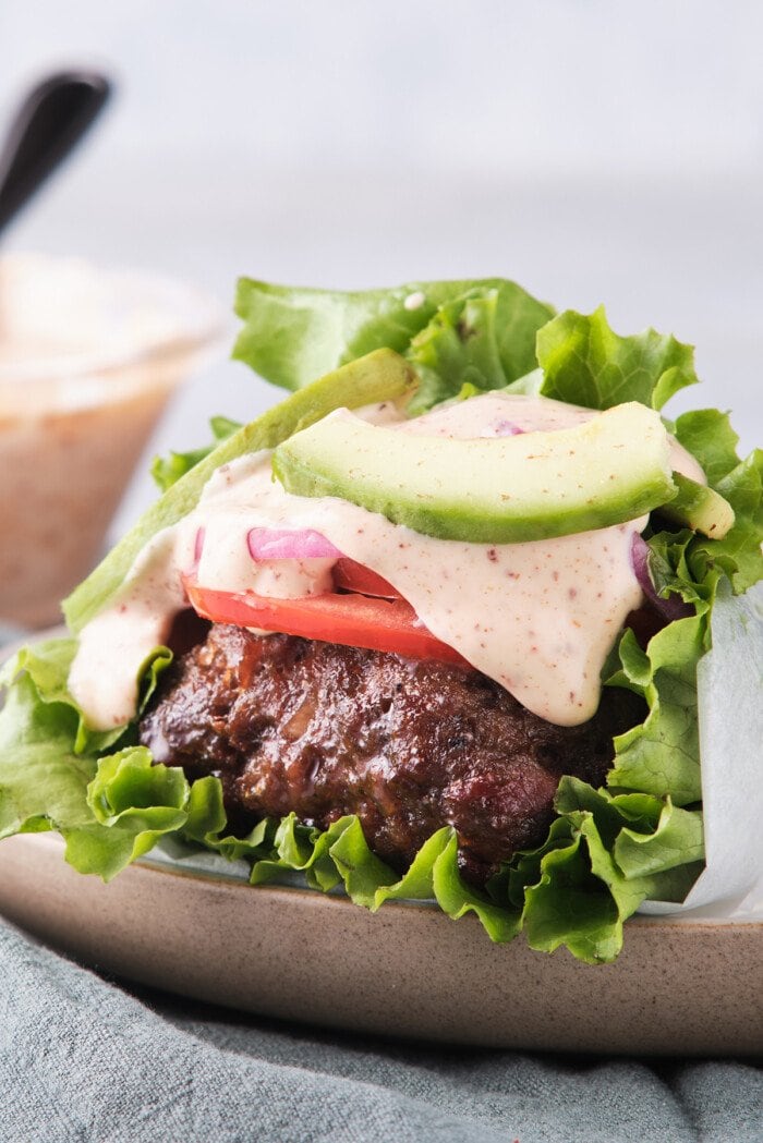 Side view of a Whole30 burger with spicy mayo wrapped in lettuce with tomatoes and red onion.