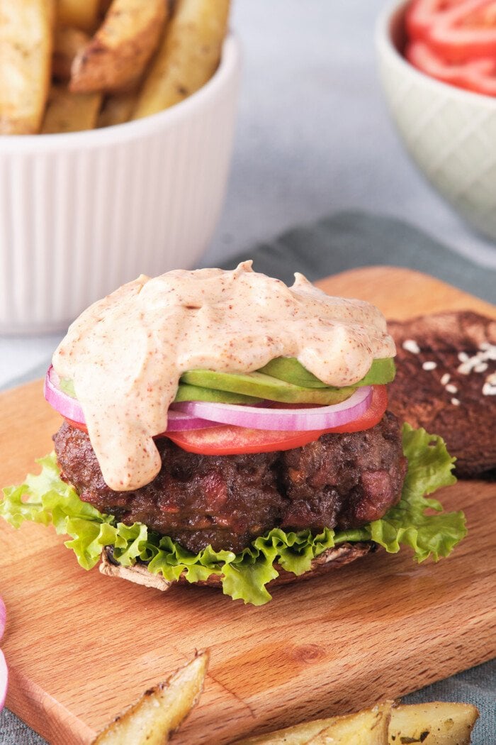 Angled, overhead view of a Whole30 burger topped with spicy mayo, onions, and lettuce on a cutting board.