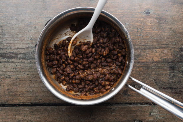 Overhead view of seasoned black beans in a large silver saucepan.