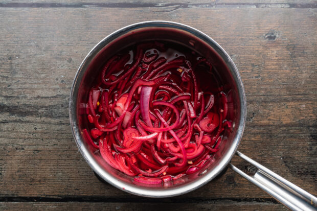 Overhead view of pickled onions in a silver saucepan.