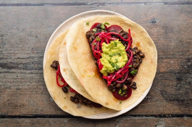 Overhead view of pickled beet tacos with black beans, onions, and guacamole on a plate.