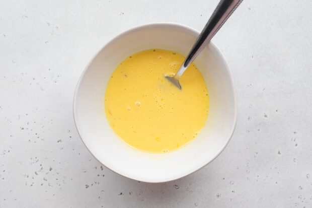 Overhead view of small white bowl with eggs and milk mixture whisked together until pale.