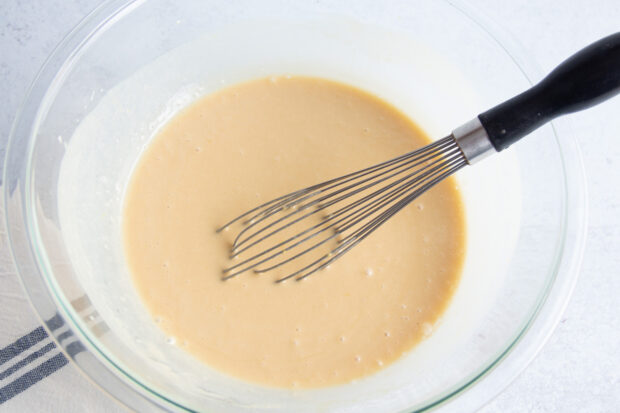 Wet ingredients for gluten free blueberry muffins in large glass mixing bowl with whisk.