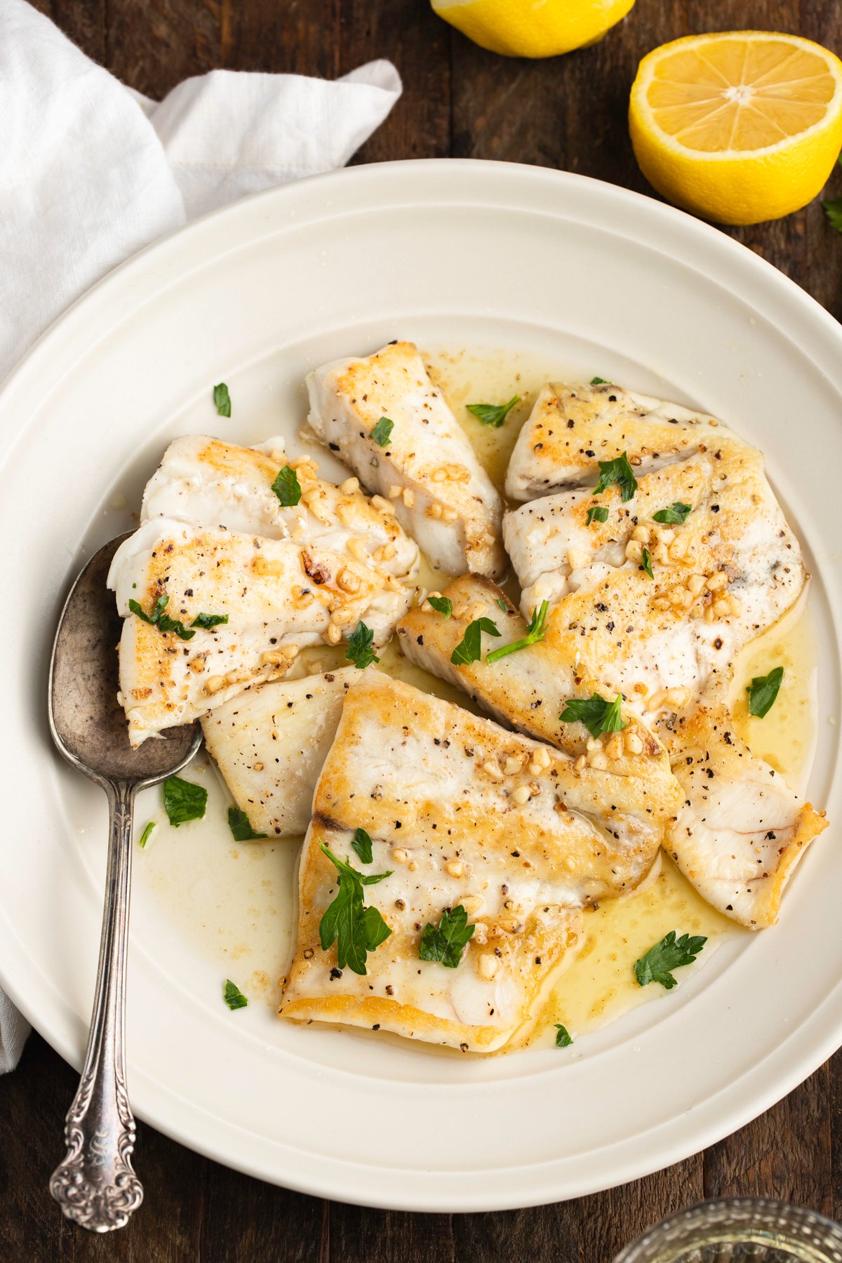 Overhead view of lemon garlic barramundi in a white bowl on a dark tabletop.