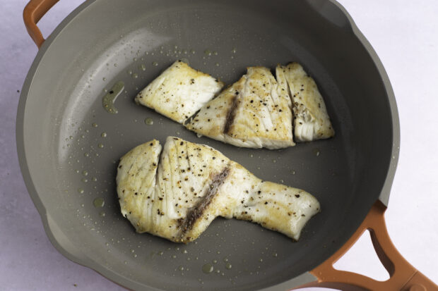 Golden brown barramundi fillets in a large skillet with olive oil.