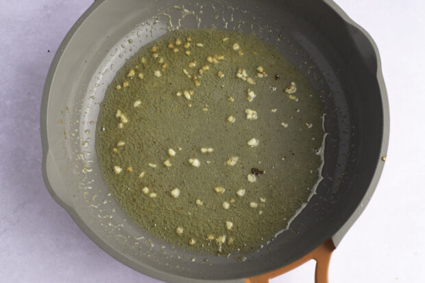 Overhead view of melted butter, minced garlic, and fresh lemon juice in a large skillet.