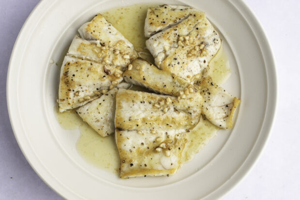 Overhead view of lemon garlic barramundi fillets in a white ceramic bowl.