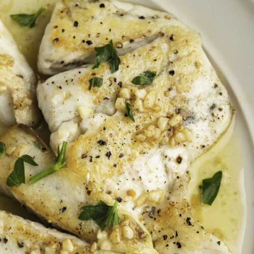 Lemon garlic barramundi in a white bowl with chopped parsley and lemon butter sauce.