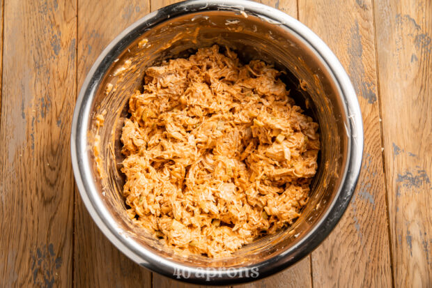 Overhead view of fully mixed BBQ chicken salad in a large silver mixing bowl on a wooden counter.