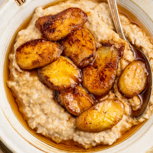 Closer, overhead view of a bowl of caramelized banana oatmeal in a white bowl on a neutral charger.