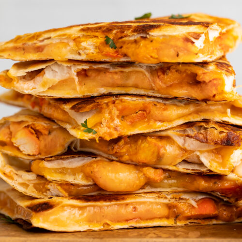 Side view of chicken tikka masala quesadillas stacked on top of each other, resting on a cutting board.