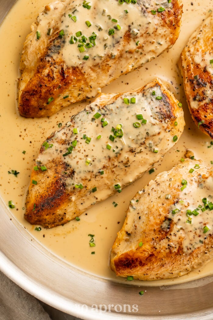 Overhead view of 3 chicken breasts in a skillet with a creamy Boursin sauce and chopped chives.