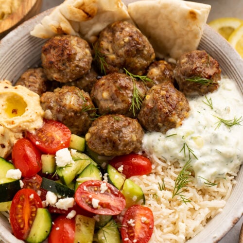 Close-up view of a bowl of cucumber salsa, gyro meatballs, lemon rice, tzatziki sauce, and naan.