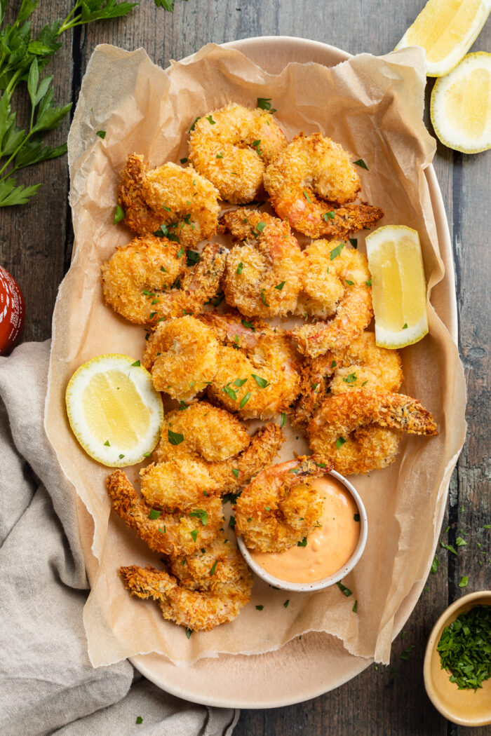 Overhead view of a platter of air fryer fried shrimp with sriracha mayo and lemon coins.