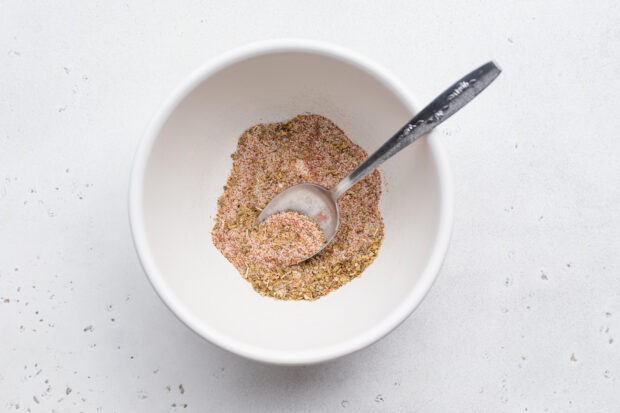 Overhead view of spice mixture for cajun fries in medium mixing bowl with a silver spoon.