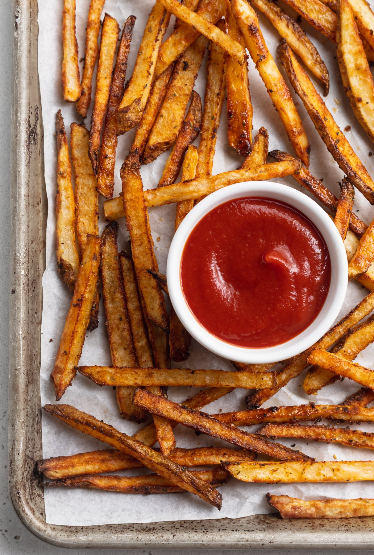 Overhead view of cajun-seasoned fries on a baking sheet with a ramekin of ketchup.