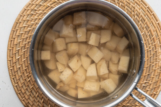 Overhead view of cubed russet potatoes in a saucepan on a neutral background.