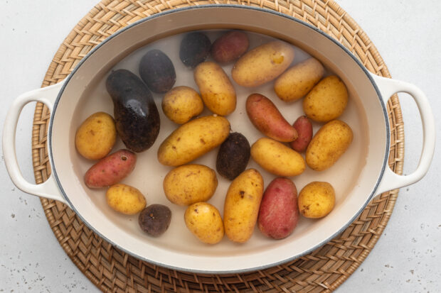 Overhead view of fingerling potatoes in a large pot with handles on a neutral background.