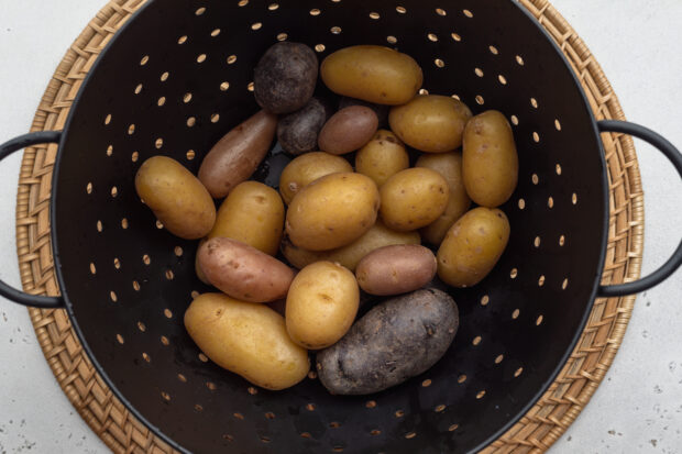 Overhead view of boiled fingerling potatoes in a large colander on a neutral background.