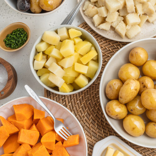 Overhead view of several varieties of boiled potatoes in bowls arranged together on a table.