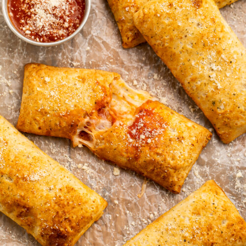 Overhead view of air fryer hot pockets (frozen and homemade) on parchment paper with pizza sauce.