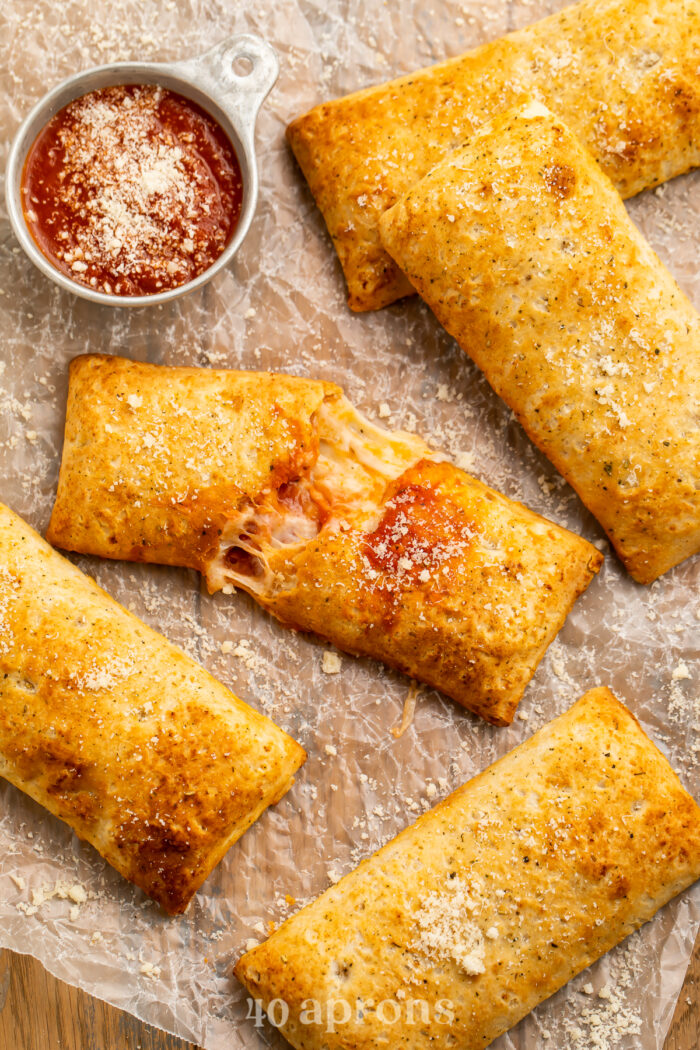 Overhead view of air fryer hot pockets (frozen and homemade) on parchment paper with pizza sauce.