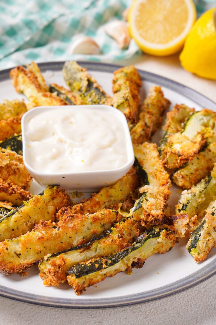 Side view of a plate of air fryer zucchini with lemons in the background.