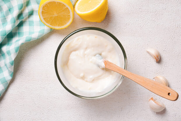 Overhead view of creamy garlic aioli in a small glass mixing bowl with a rubber spatula.