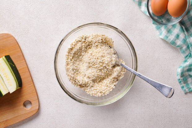 Overhead view of breadcrumb mixture in a medium glass mixing bowl with a fork.