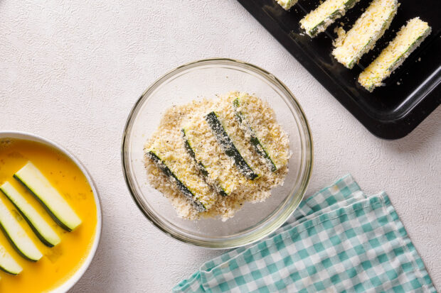 Overhead view of zucchini sticks in glass mixing bowl with breadcrumb mixture.