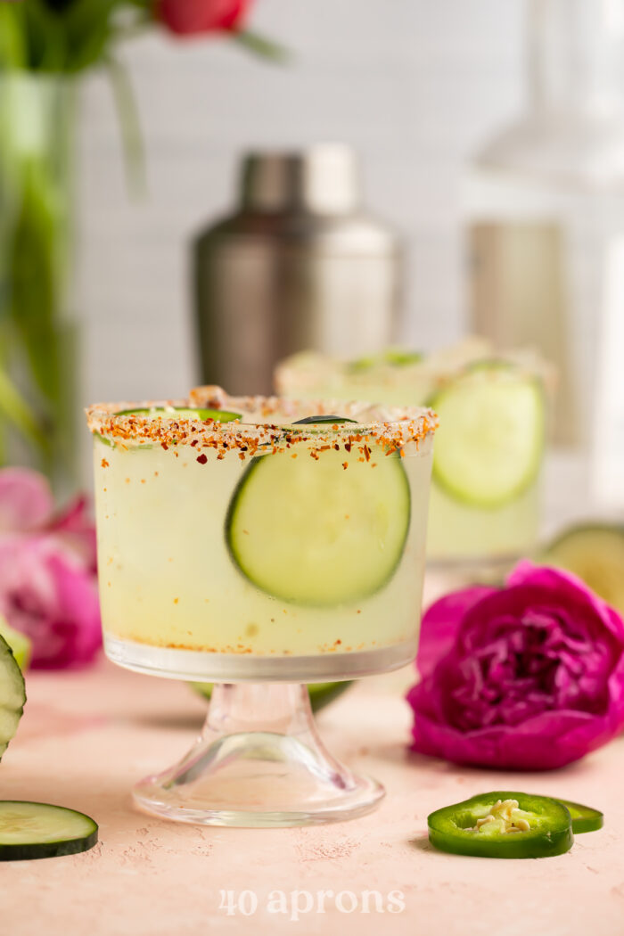 Cucumber jalapeno margarita in a short glass with cucumber slices and a deep fuschia flower.