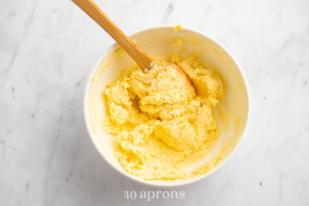 Overhead view of garlic butter sauce mixture in a white bowl with a wooden spoon.