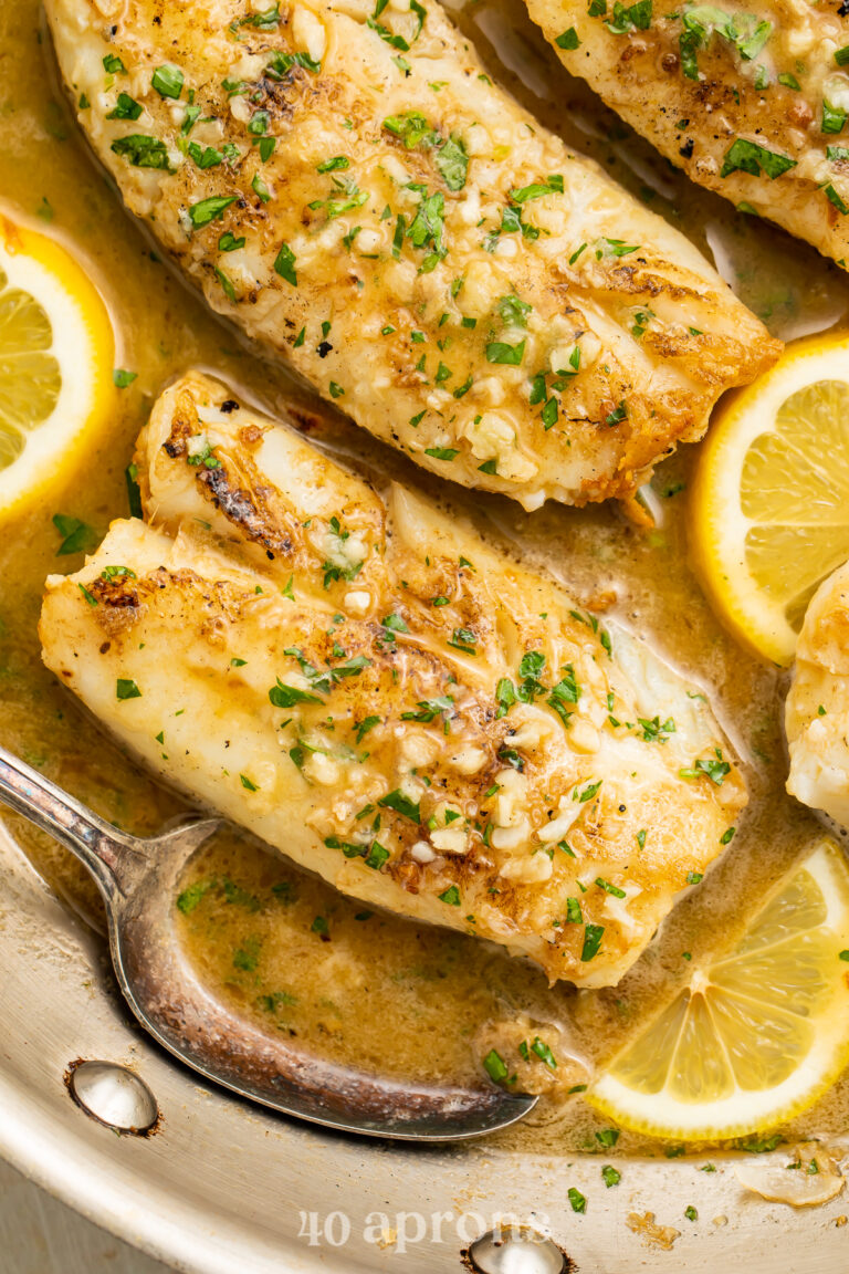 Overhead view of garlic butter cod filets in a silver skillet with garlic butter sauce and lemon coins.