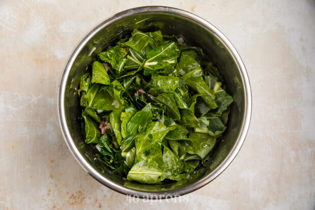 Overhead view of collard greens, bacon, onions, garlic, and chicken broth in Instant Pot.