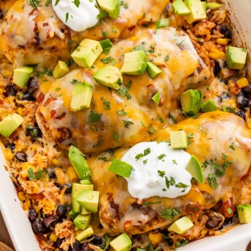 Overhead, angled view of a Mexican chicken and rice casserole with corn, black beans, sour cream, and diced avocado.