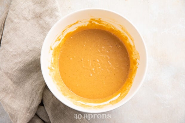 Overhead view of Thai peanut chicken sauce in a white mixing bowl on a marble tabletop.