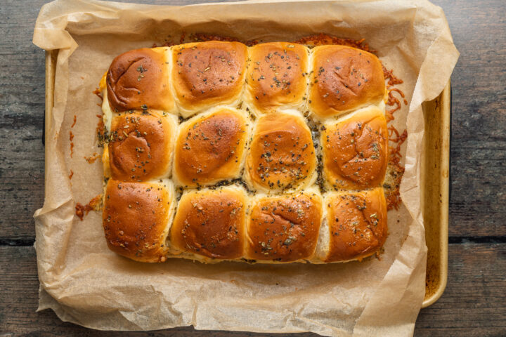 Overhead view of browned, baked buffalo chicken sliders in a baking dish lined with parchment paper.