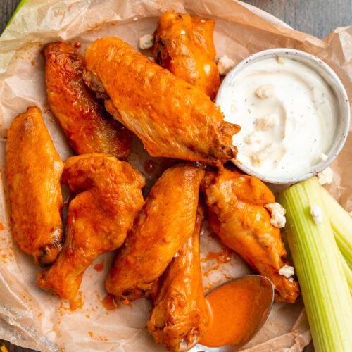 Overhead view of a plate piled high with orange chicken drumsticks and flats, next to a small ramekin of ranch dressing.