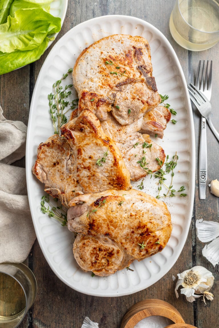 Overhead view of four sous vide pork chops arranged on an oval white platter on a dark wood tabletop.