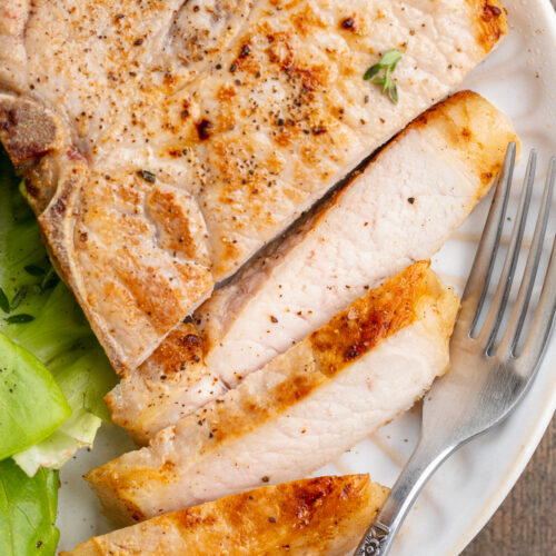 Overhead view of a sliced sous vide pork chop on a white plate with a simple green lettuce salad.