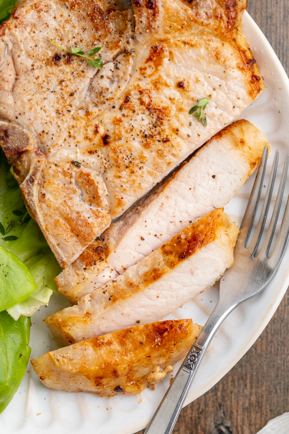 Overhead view of a sliced sous vide pork chop on a white plate with a simple green lettuce salad.