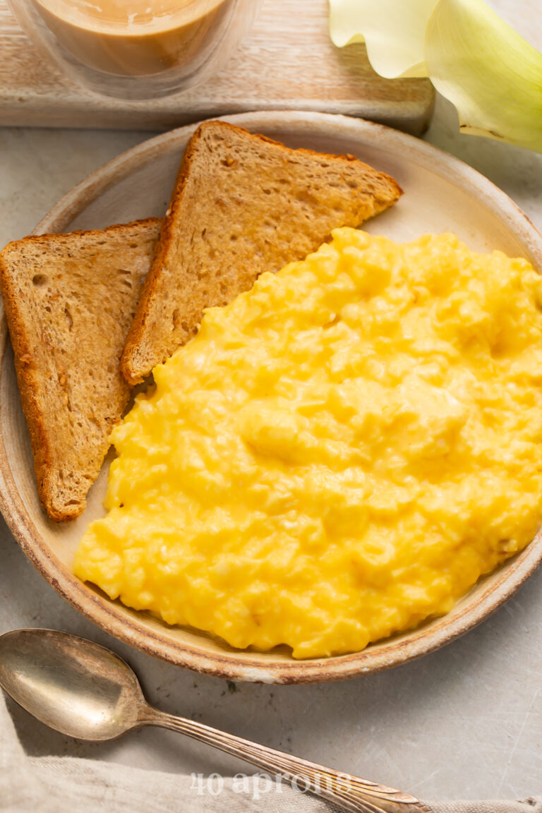 Overhead, angled view of a bowl of mom's favorite cheesy scrambled eggs with two triangles of toasted whole grain bread.